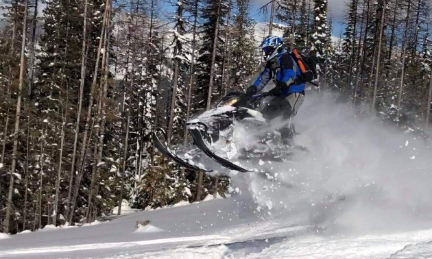 A snowmobiler gets air going downhill. 