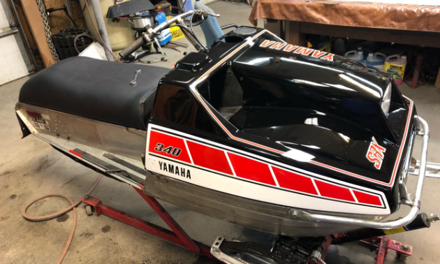 This black vintage snowmobile has red squares along the side with a white stripe underneath 