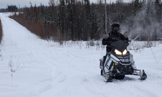 A snowmobiler dressed in black on a black snowmobile rides along a trail in the snow. 