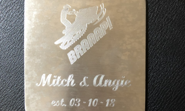 A golden coaster with a snowmobiler on it that says Mitch & Angie. 