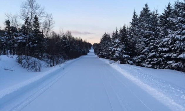 A long, wide trail is groomed for snowmobiles to ride on.