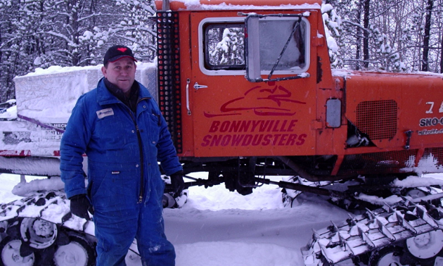 Angus Ross stands next to a snowmobile groomer.
