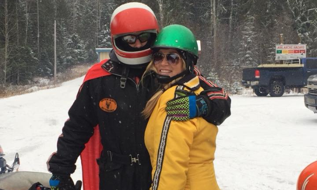 Matt Elliott and Sara Olofsson hug while wearing retro snowmobile gear.