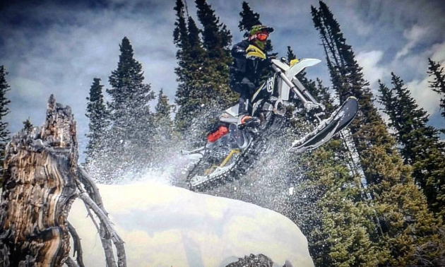 A white and black snow biker launches out over the camera for a wicked photo. 