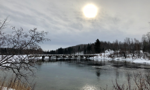 The sunshine casts light on a lake with a bridge in the distance