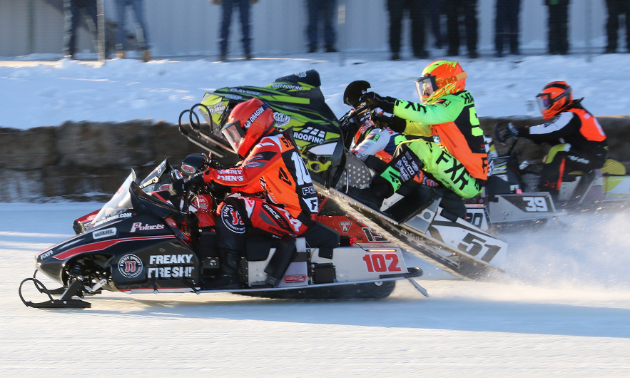 A side view of several snowmobile racers that are neck and neck with each other.