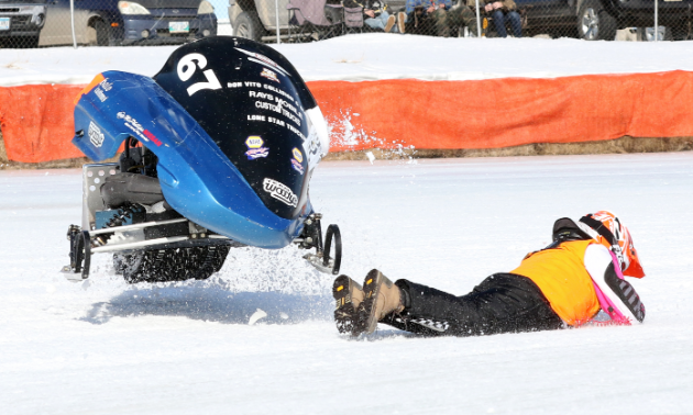 A snowmobiler is thrown from her sled as it skips into the air.