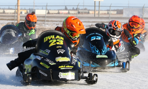 Five children race snowmobiles around a track.