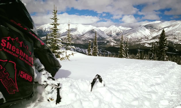 A black and red snowmobile is pointed towards the distant mountains.