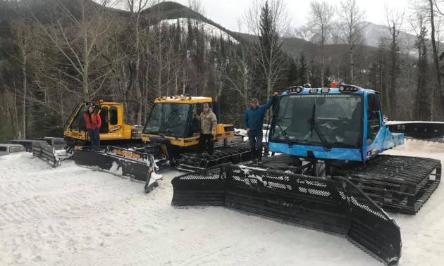 Three snowcat groomers line up next to each other on top of snow.