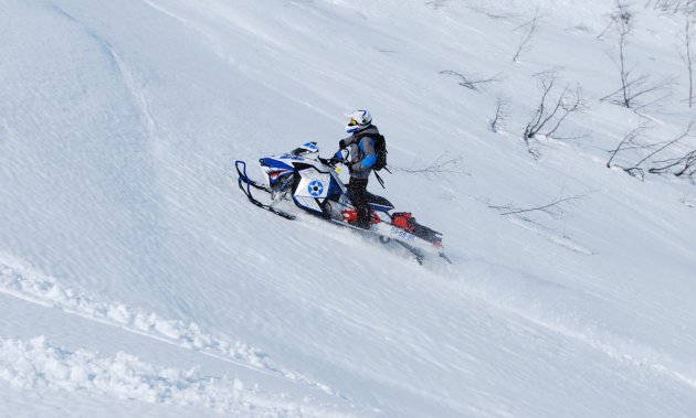 A snowmobiler climbs up the side of a mountain.