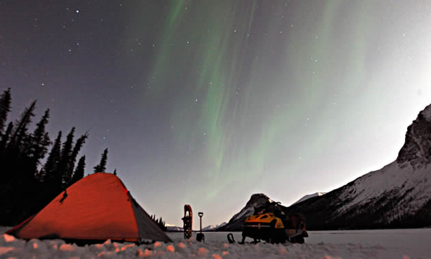 A tent, snowmobile and northern lights in the mountainous Fort St. John area.