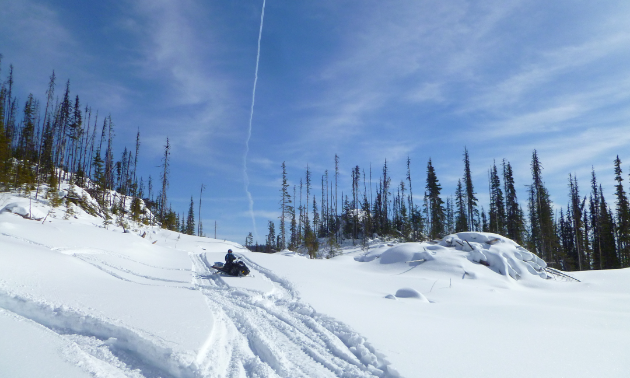 A snowmobiler parks on a trail under a blue sky.