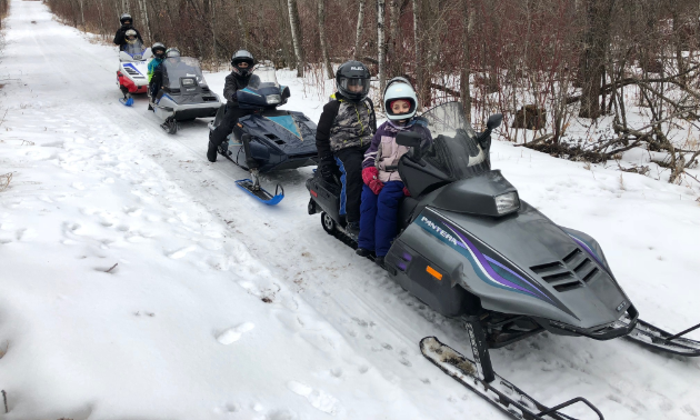 Kids ride vintage snowmobiles on a trail in Manitoba.