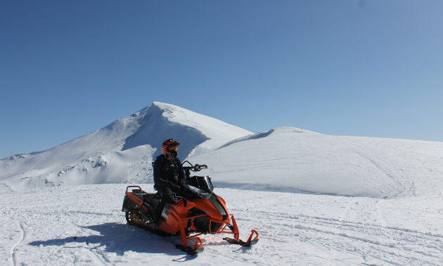 A sledder stopped with two mountain peaks in the background.