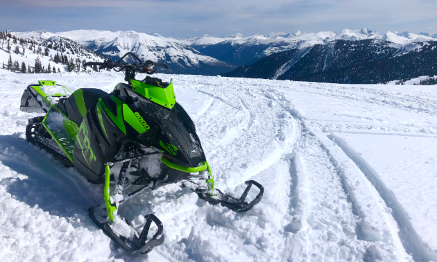 A green and black 2018 Arctic Cat M8000 Mountain Cat 153” is parked in the snow on top of a mountain.