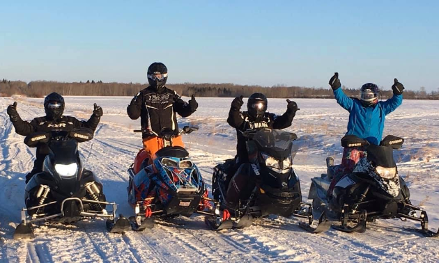 Four snowmobilers throw up their hands in a happy pose.