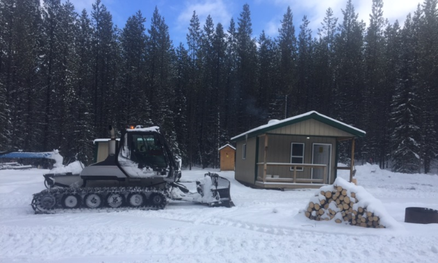 A snowmobile groomer is parked next to the Swartz Creek Cabin.