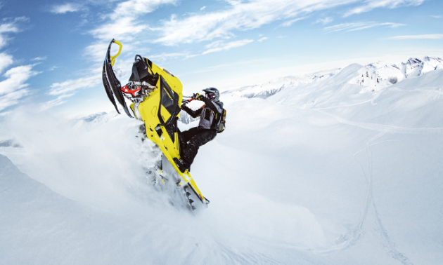 A snowmobiler climbs a mountain on a yellow Ski-Doo Summit 850 E-TEC.