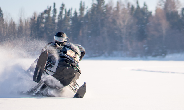 A snowmobiler gets air in a field.