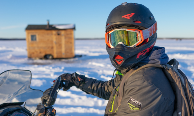 A snowmobiler stops near a warm-up shelter.