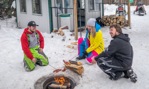 Ashlyn George and her friends enjoy a hot dog roast by a fire next to a warm-up shelter.