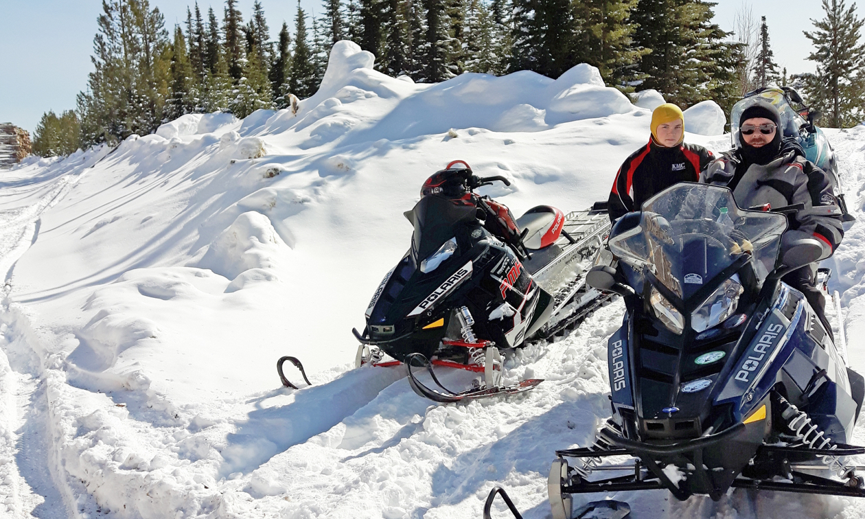 A couple of riders take a break on their snowmobiles. 