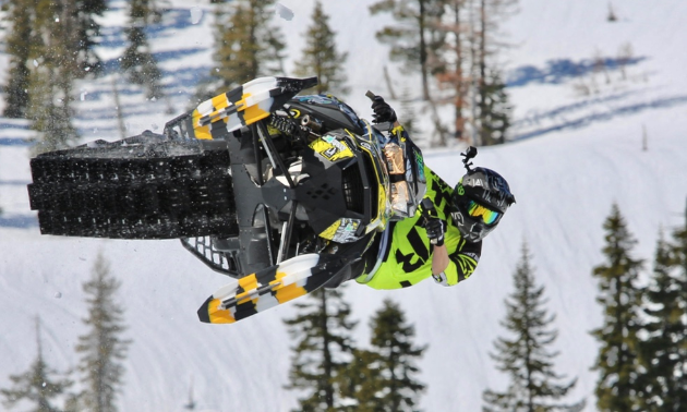 A green snowmobiler has his sled sideways in the sky. 