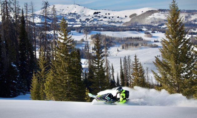 A snowmobiler rides through fresh powder at the foothills of mountains.