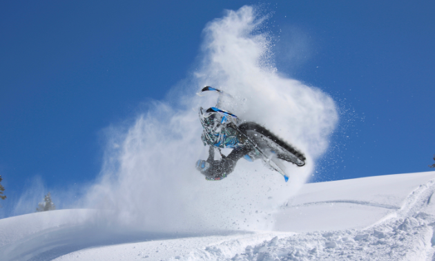 A snowmobiler gets air with a blue sky backdrop. 