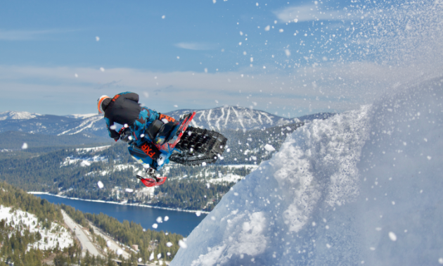 The back of a snowmobiler as he jumps off a mountain. 