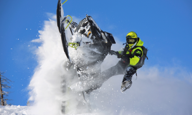 A snowmobiler gets vertical with a plume of snow all around him. 