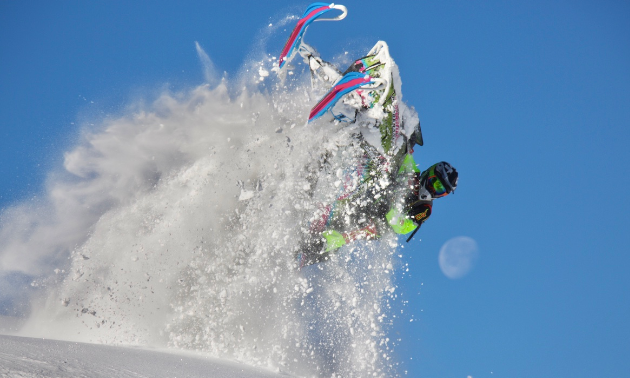 A snowmobiler jumps towards the camera with snow billowing underneath his sled.