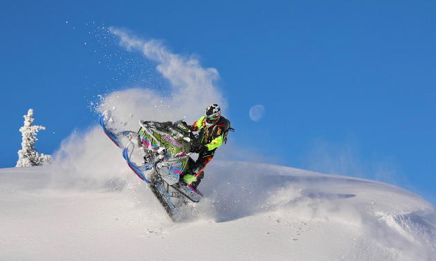 A cloudy trail of snowy smoke trails behind a snowmobiler on a sunny day.