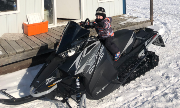 A small child sits on a full-sized black snowmobile.