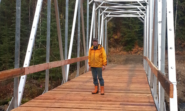 A man stands on a wooden bridge with metal framework holding it together.