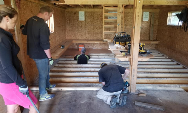 Workers are on their knees refinishing a floor in a cabin.