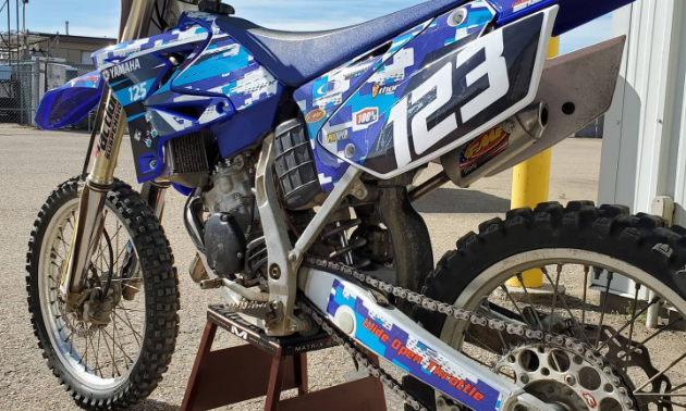 A dirt bike with a blue and white wrap and the numbers 123.