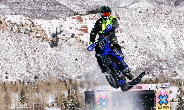 A blue snow bike gets massive air at an X-games competition.