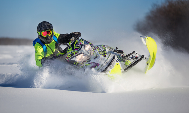 A snowmobiler leans sharply into a turn.