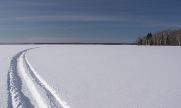 A large, open plain of snow has a single track leading through it. 