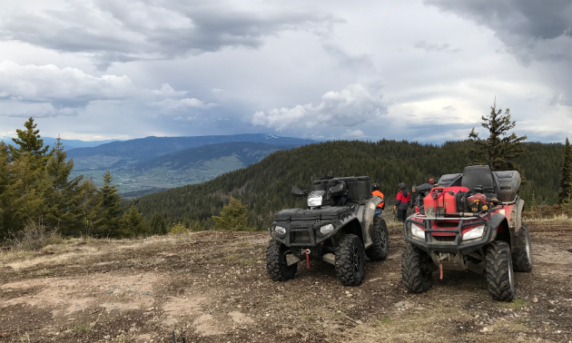 Two ATVs sit on top of a mountian. 