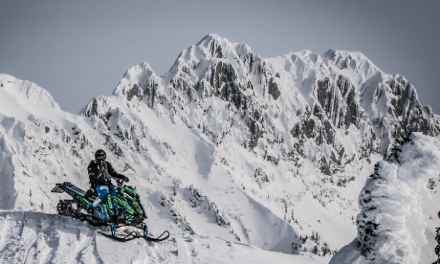 Logan Thibodeau poses with his snowmobile on a mountainside