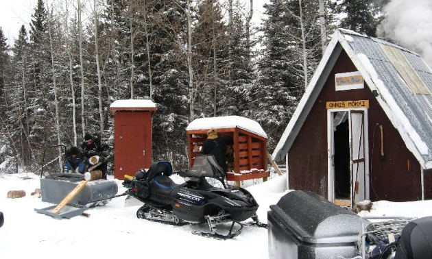 A warm-up shelter is pictured with snowmobiles parked in front of it. 