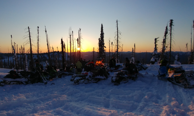 Snowmobilers gather for a bonfire at sunset