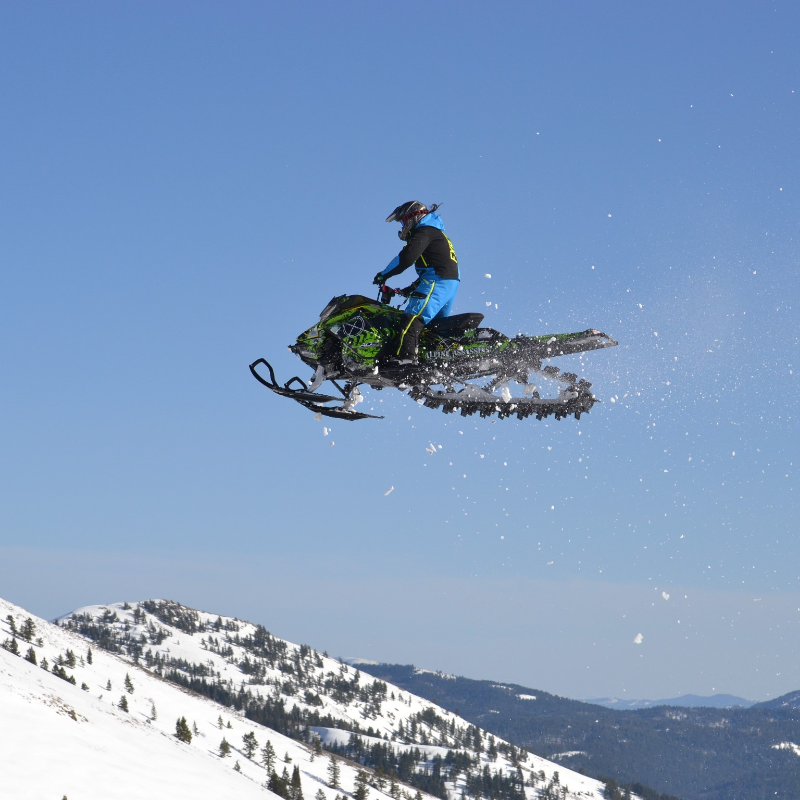 Alonzo Coby flies through the air in the mountains on a snowmobile. 