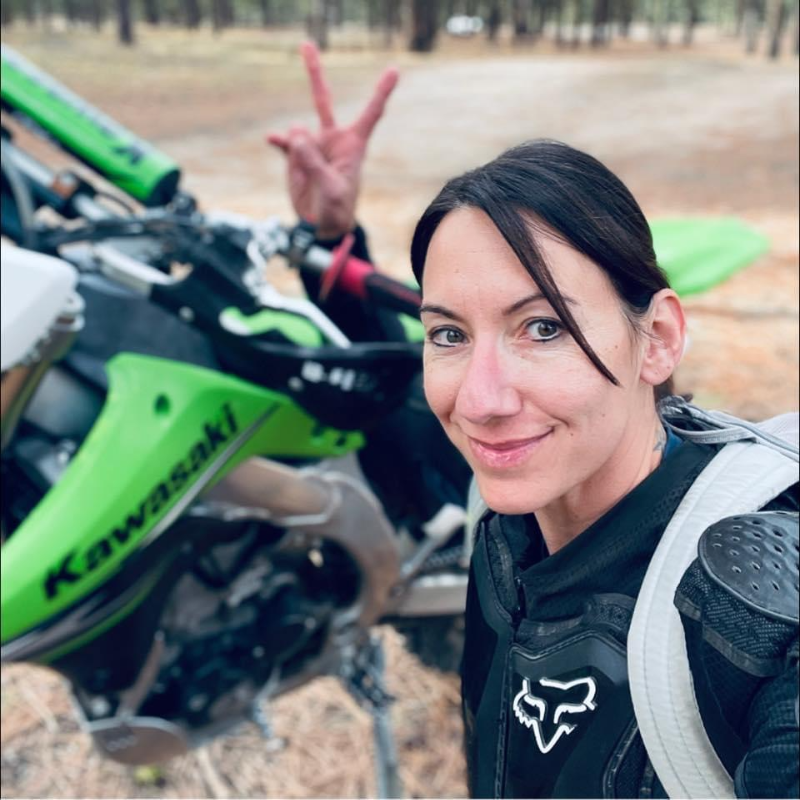 Alysha “Axxe” Vlahovich smiles next to her green Kawasaki dirt bike. 