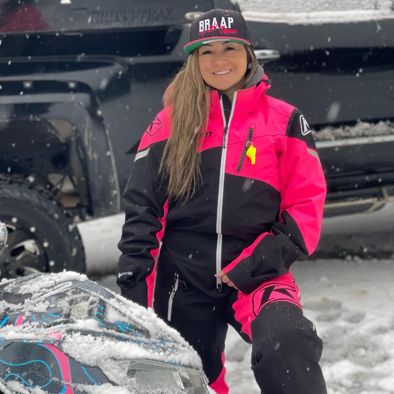 Jenny Hashimoto-Wiebe smiles in front of a black truck. She wears a pink and black jacket and a hat that says Braap.