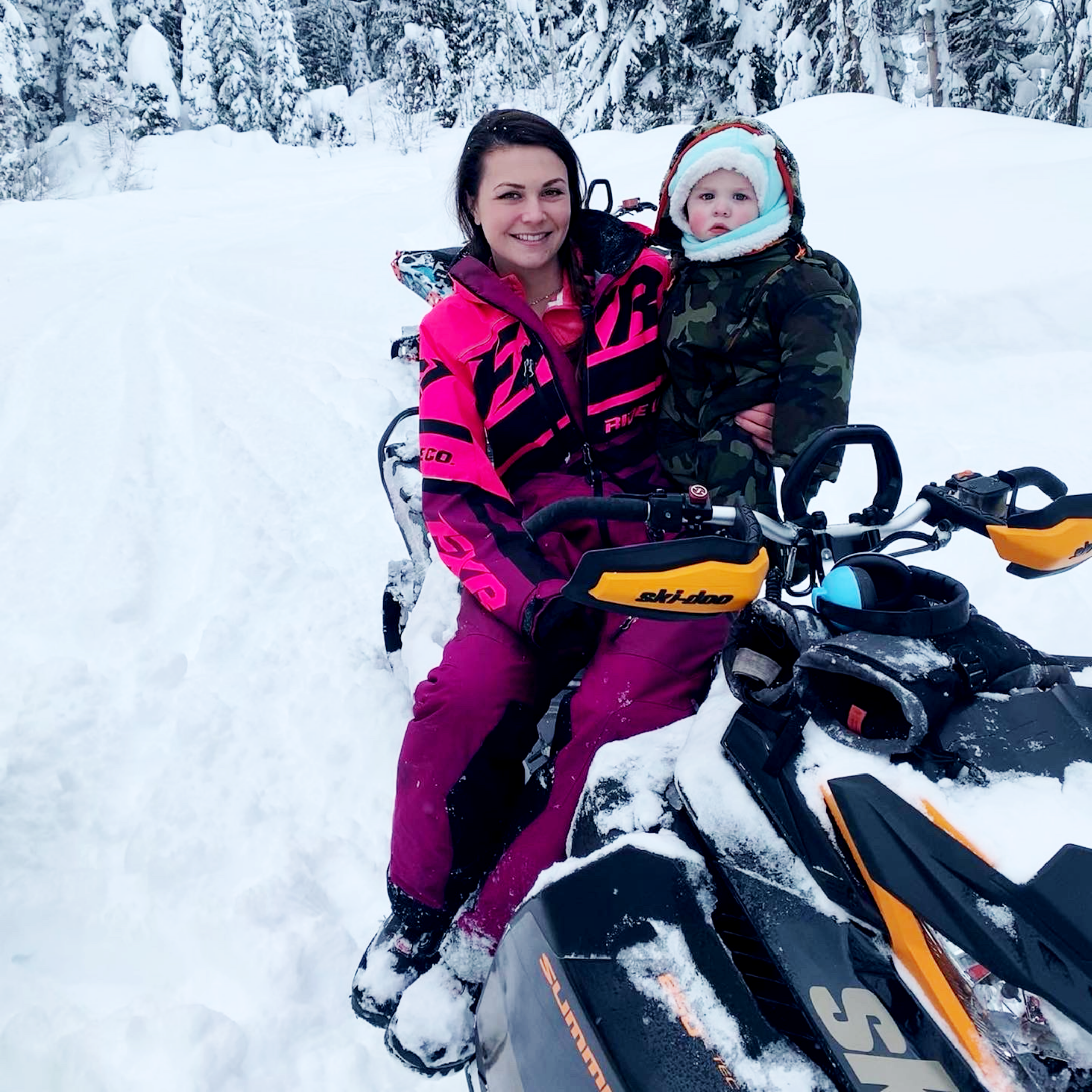 Shelby Ingram wears a pink snowsuit while sitting on a snowmobile with her one-year-old son, Mason Chomica.