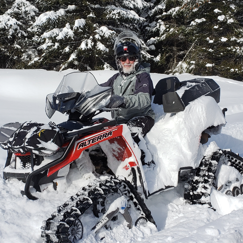 Wayne Mercer rides a red and black 2017 Arctic Cat Alterra XT TRV 1000 with tracks through deep snow.